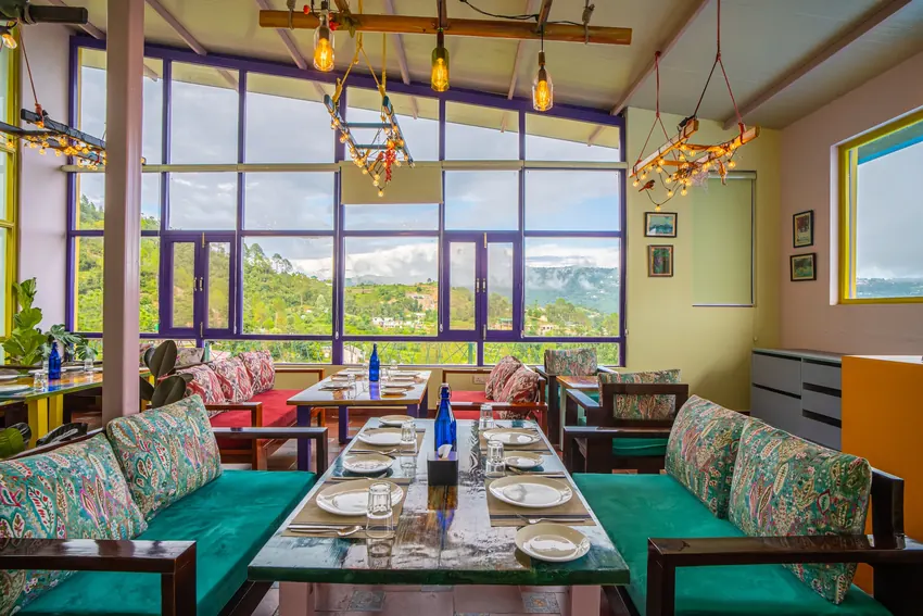Restaurant tables and chairs set next to valley view glass windows at Buransh